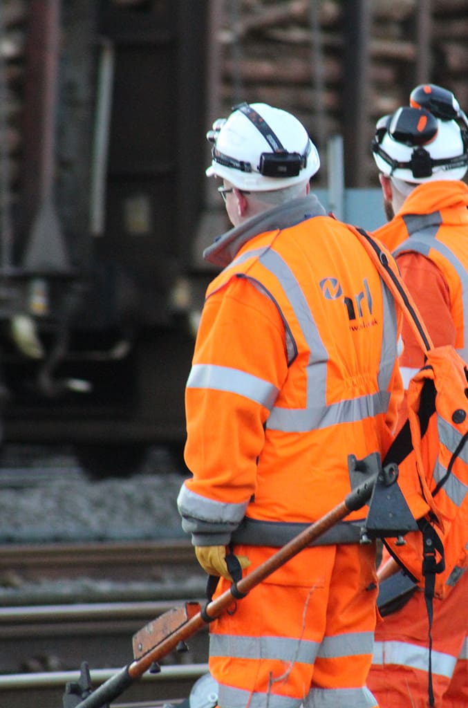 2 NRL rail contractors stood looking at a railway track, both wearing full orange PPE