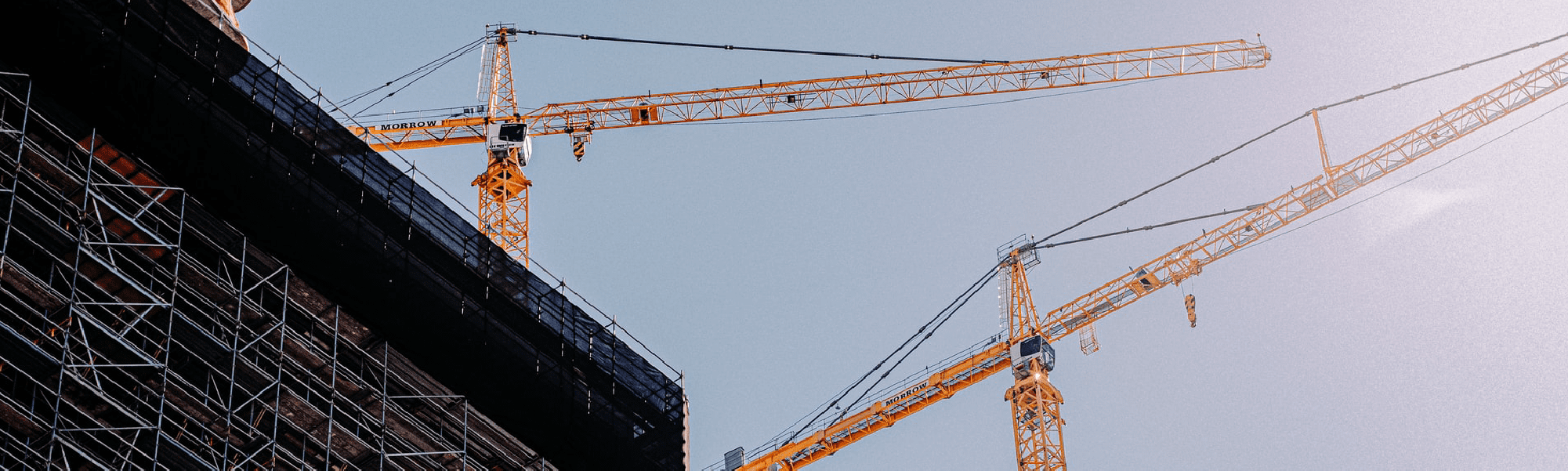 A perspective view of 2 large yellow cranes, picture taken from below