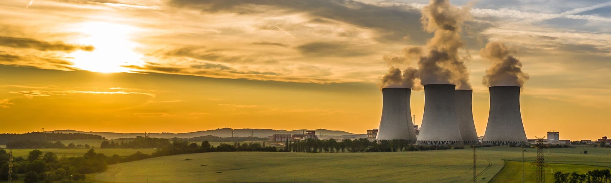 A picture of a nuclear power plant - 4 cooling towers visible and a sunset background