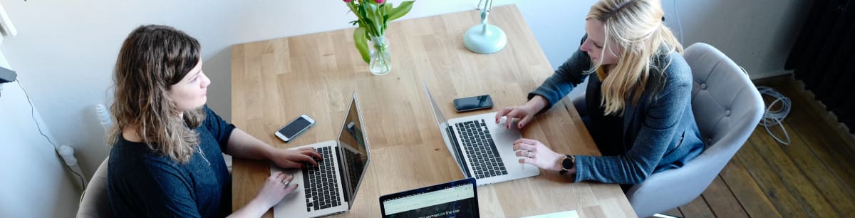 2 women sat opposite each other at a desk, both working on their laptops