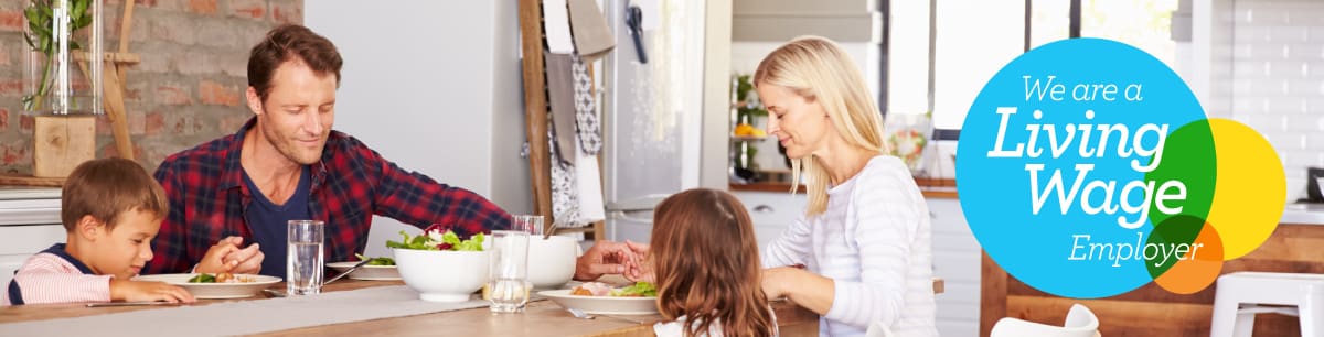 A picture of a family enjoying a meal at home with the Living Wage Employer logo on the right side of the image