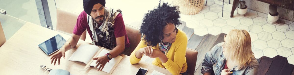 An aerial view of a 3 diverse colleagues sat round a meeting table