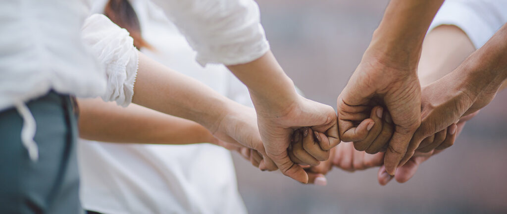 Four hands link together in pairs, showing connection, support and teamwork.