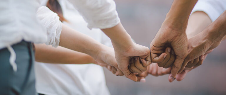 Four hands link together in pairs, showing connection, support and teamwork.