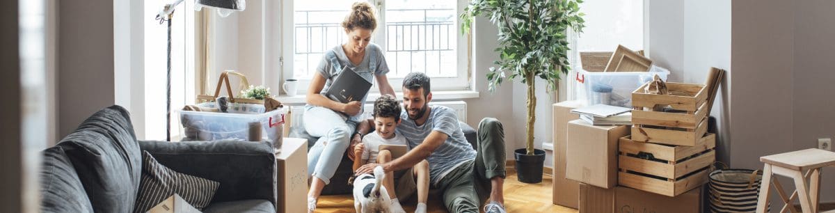 A family grouped together on a sofa surrounded with moving boxes, stroking their dog.