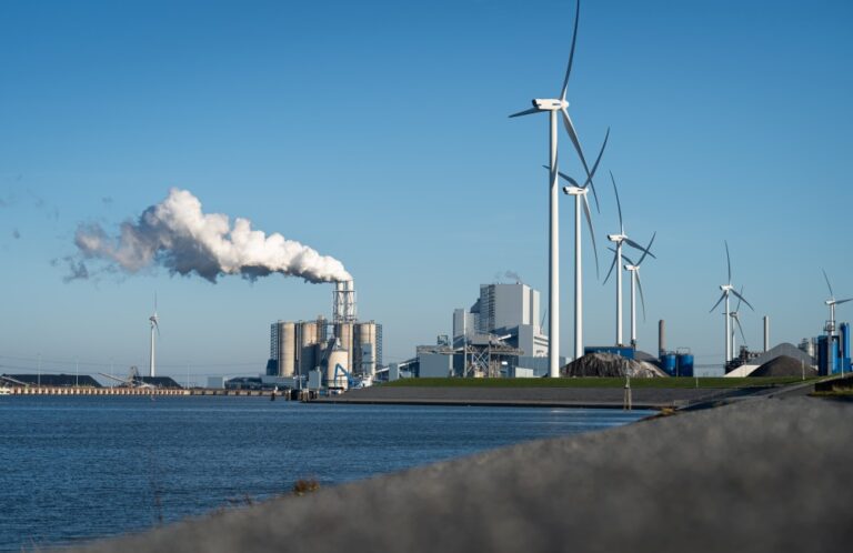 Industrial power plant with cooling towers emitting steam across farmland under a clear sky.