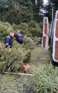 Jack Gannon from Heysham Branch collects Christmas trees with a volunteer, wearing blue overalls by a white van.