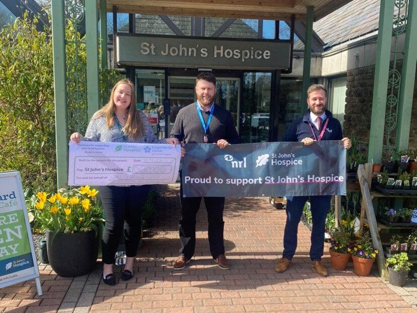 Jack and Nick from the Heysham branch stood holding an NRL banner in front of St John's Hospice after donating £500.