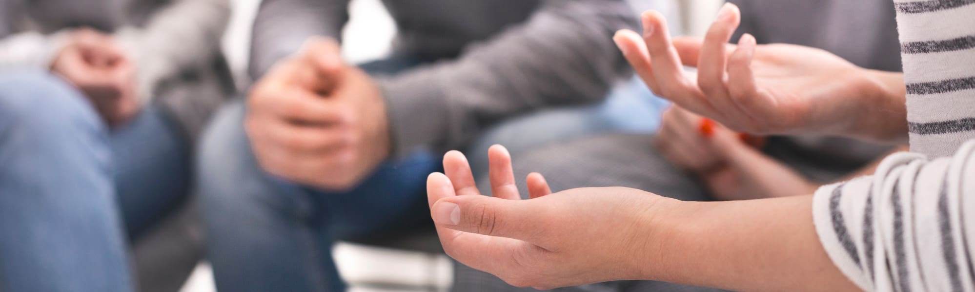 A group of people in a counseling session, focus on one woman's hands