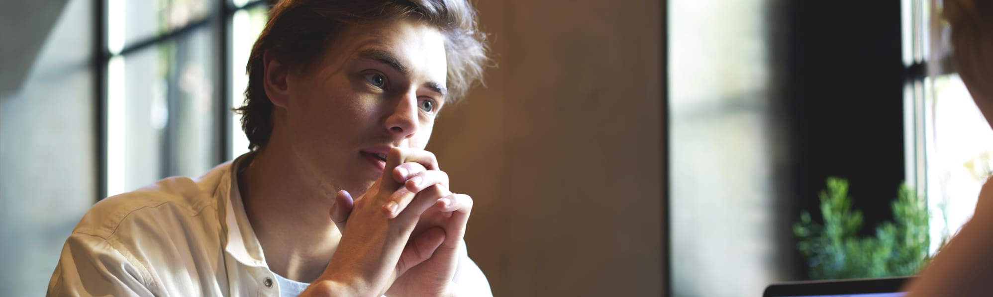 A man with hands resting on his chin, talking to someone opposite him, out of the frame.