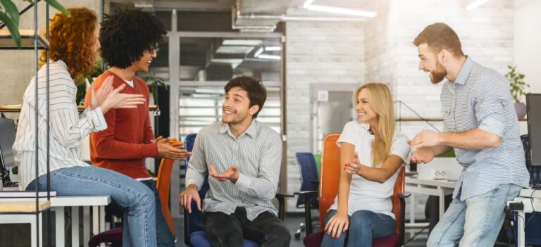 Five people sit and stand together, talking and gesturing during a discussion in an open workspace.