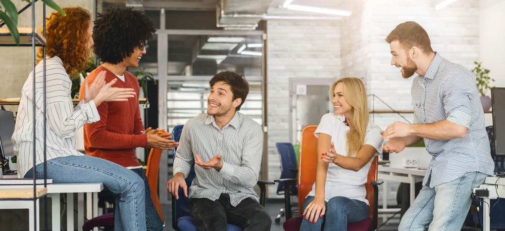 Five people sit and stand together, talking and gesturing during a discussion in an open workspace.