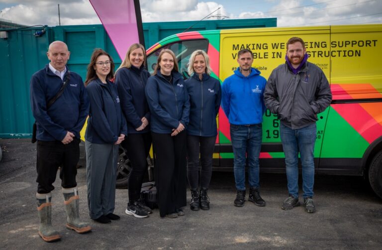 Seven people stand beside a brightly coloured vehicle with wellbeing support text on the side.