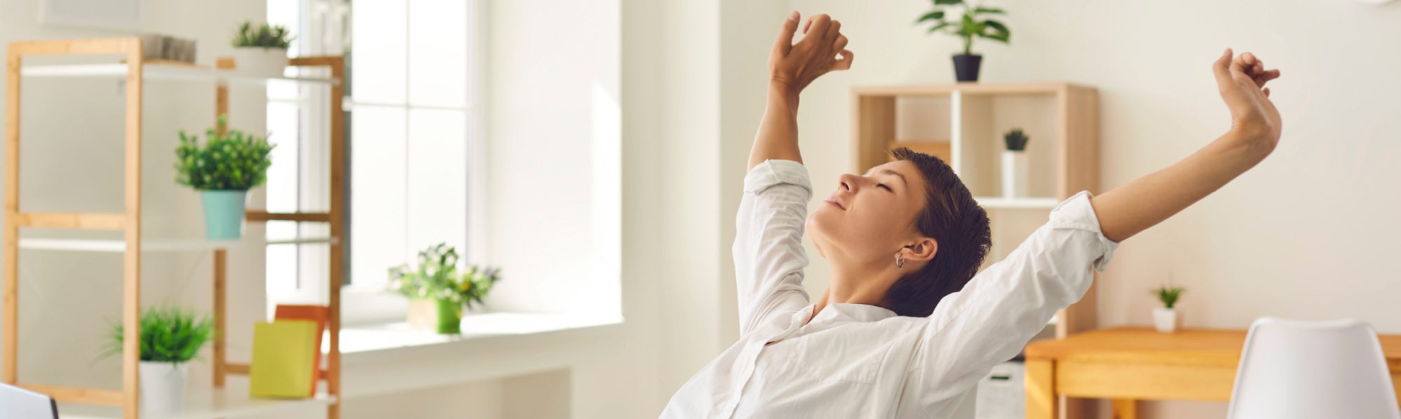 Woman leaning back on chair, arms above head, eyes closed, appearing relaxed.