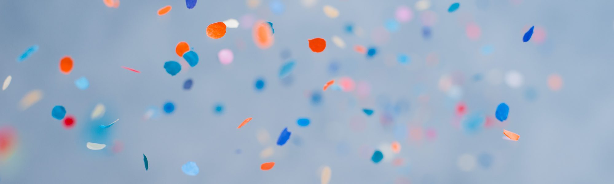 Colourful confetti falling against a pale blue background.