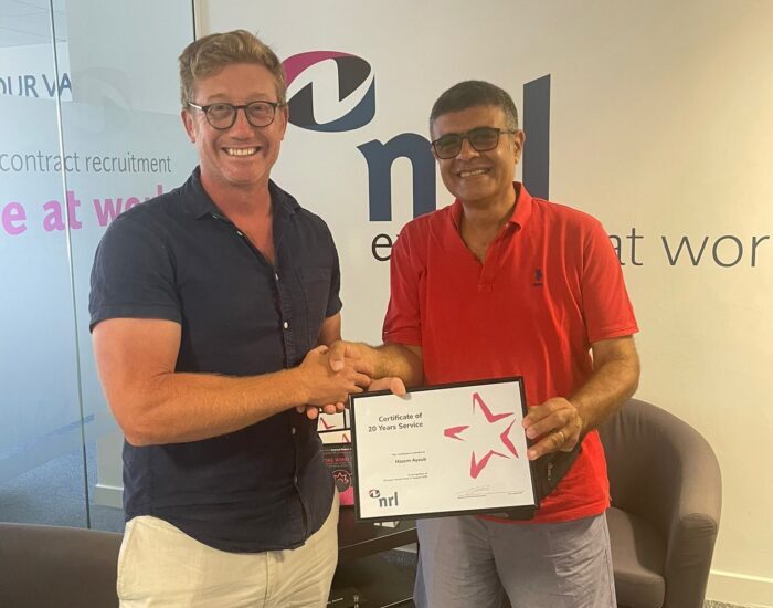 Two people shake hands while holding a framed certificate in front of a wall with NRL branding.