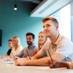 Group seated at a table listening and taking notes during a training session in a meeting room.
