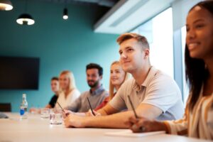 Group seated at a table listening and taking notes during a training session in a meeting room.