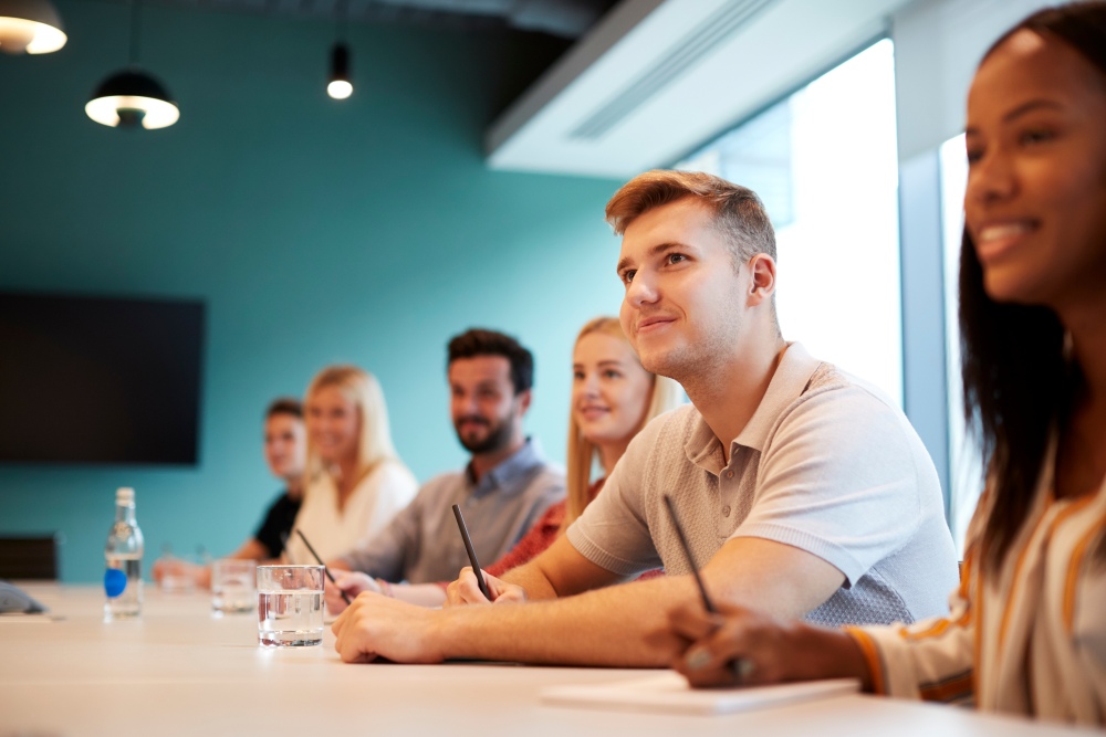 Group seated at a table listening and taking notes during a training session in a meeting room.