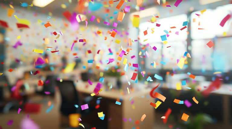 Colourful confetti falling in an office setting with desks and chairs blurred in the background.
