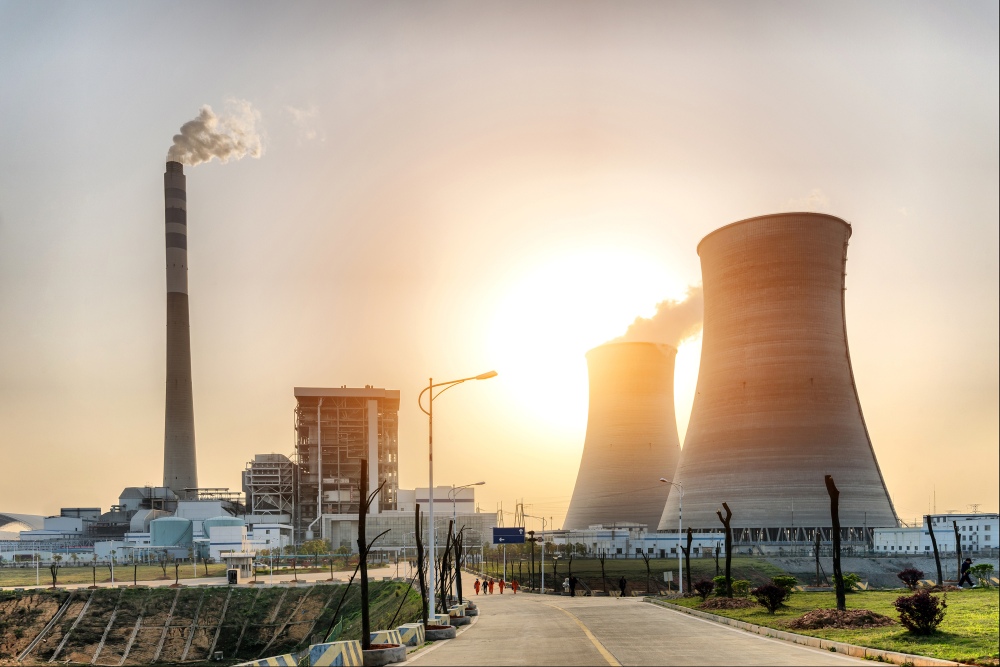Industrial power plant with cooling towers and chimney emitting smoke at sunset.