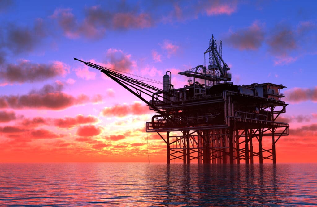 Offshore platform stands in the sea at sunset with structure silhouetted against the sky.