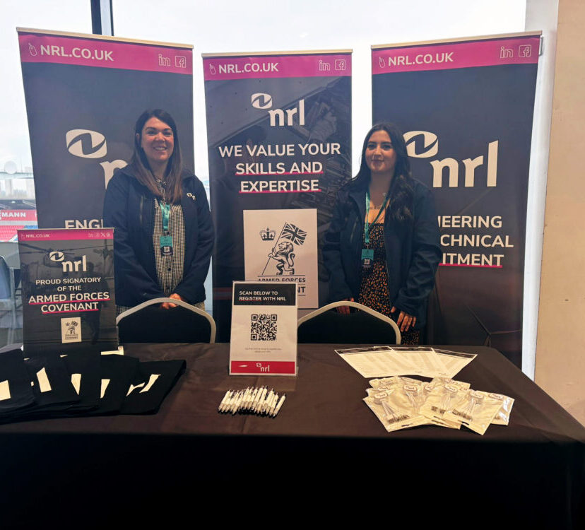 Two people stand behind an NRL branded stand displaying leaflets, tote bags and QR code sign.