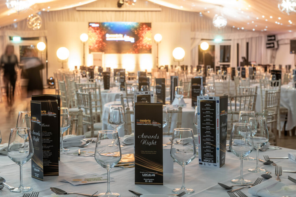 Banquet hall with round tables, place settings and menus prepared for an awards event.
