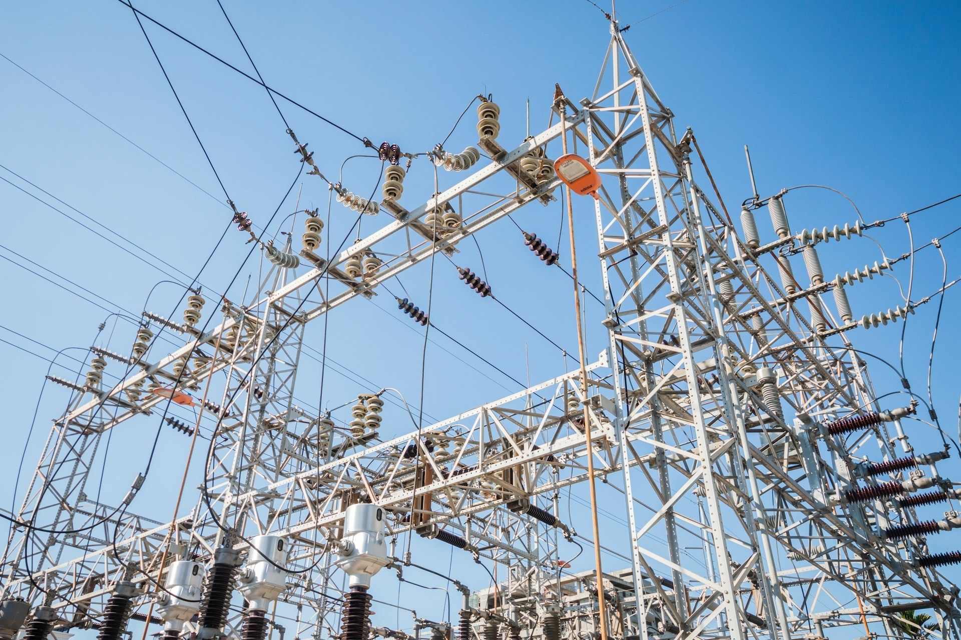 Electrical substation with steel structures, cables and transformers against a clear sky.