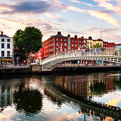 Arched pedestrian bridge over a river with red brick buildings and reflections in the water.