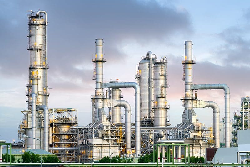 Large industrial plant with tall towers, pipes and processing units under a cloudy sky.
