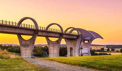Large rotating boat lift structure spans a canal above a grassy landscape at sunset.