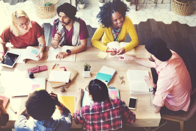 Overhead view of six people sitting around a table reading books and discussing work together.