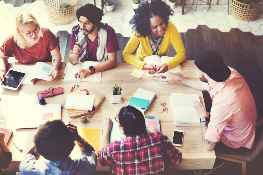 Overhead view of six people sitting around a table reading books and discussing work together.