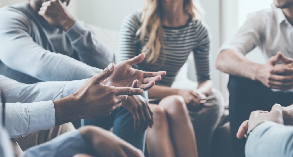 Close-up of people seated together, gesturing with hands while participating in a group discussion.
