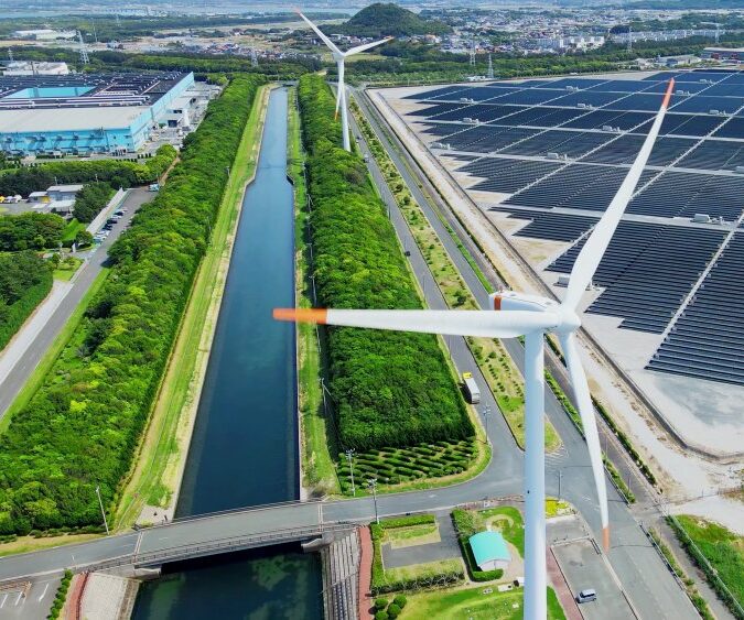 Aerial view of wind turbines and solar panels beside a canal in an industrial area.