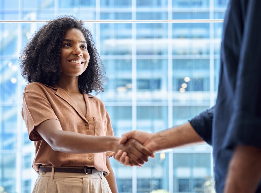Two people shake hands in front of a glass building, marking a business agreement.