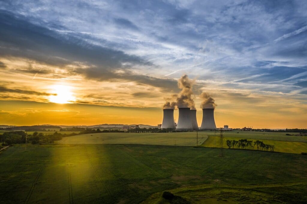 Three cooling towers emit steam across farmland under a colourful sunset sky.