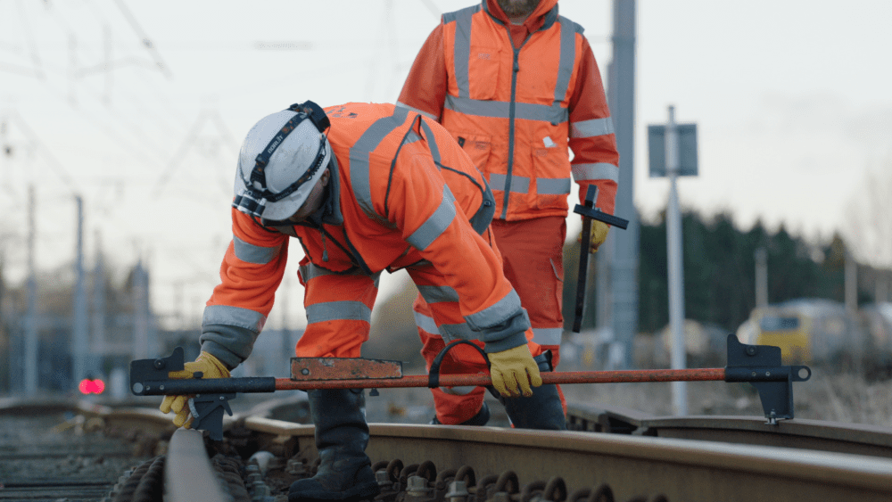 Two workers in high-visibility clothing adjust railway tracks using tools during maintenance.