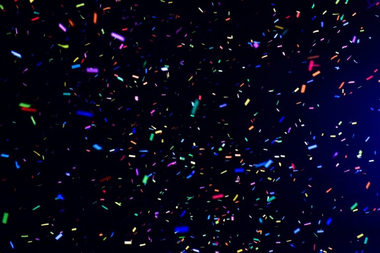 Multicoloured confetti pieces scattered and falling across a dark background.