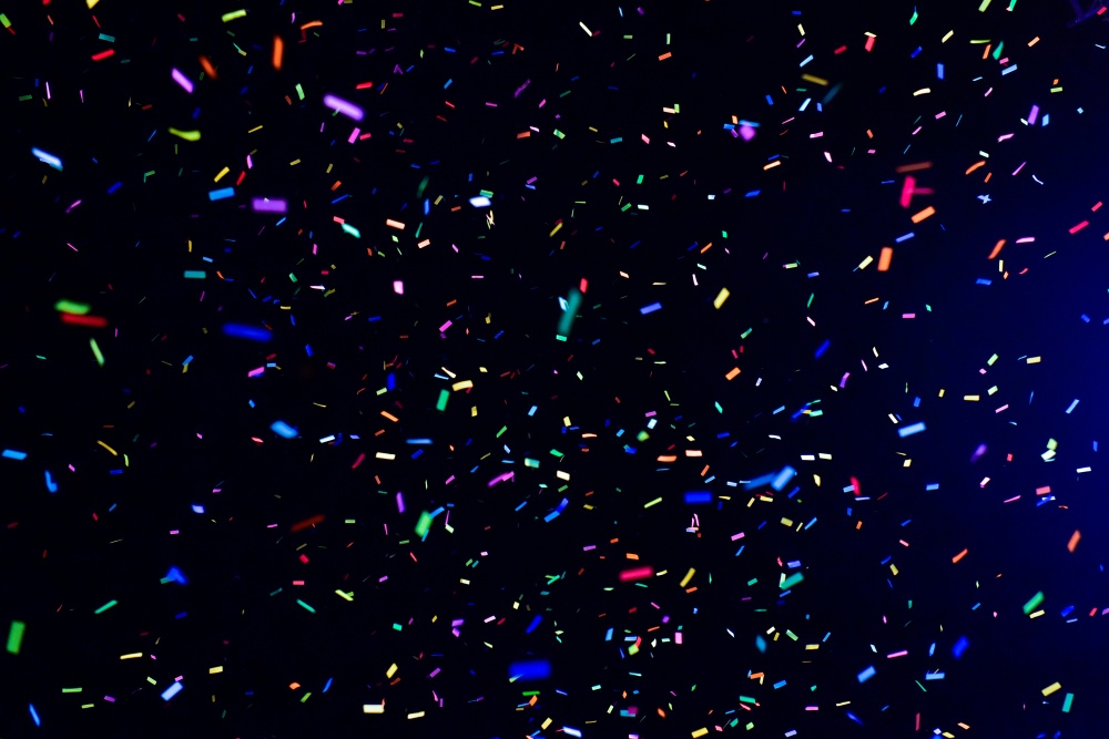 Multicoloured confetti pieces scattered and falling across a dark background.