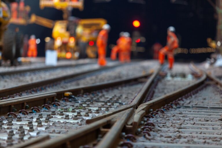 Railway workers in high-visibility clothing stand on tracks during maintenance with equipment nearby.