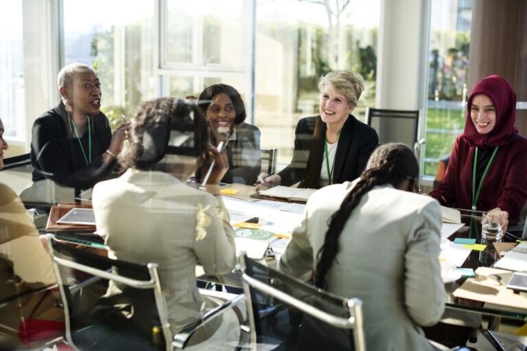 Group seated around a table, discussing work with papers, laptops and drinks in a meeting room.
