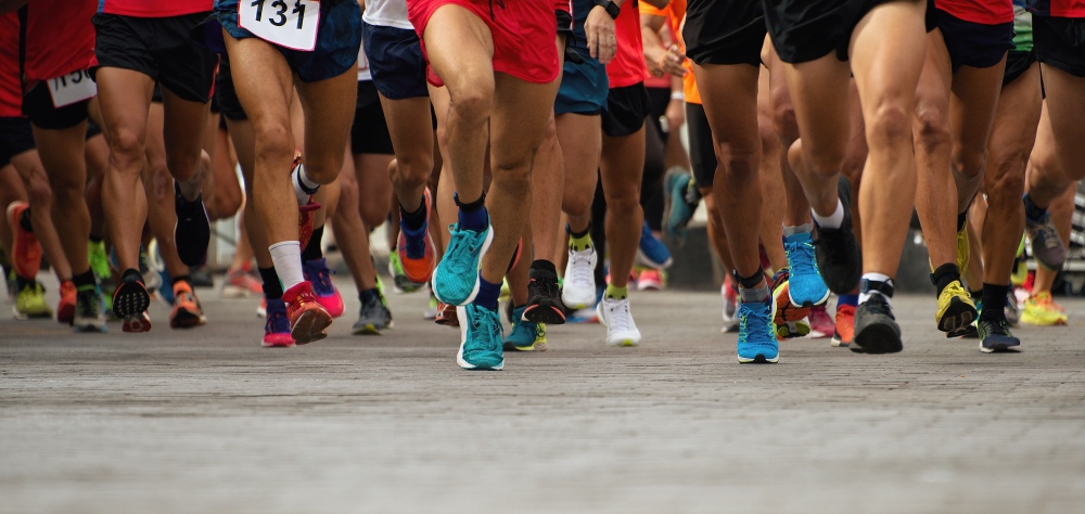 Close-up of runners’ legs and trainers moving together during a road race event.