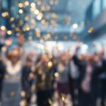 Gold confetti falls over a crowd gathered indoors during a workplace celebration or event.