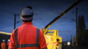Worker in high-visibility clothing and hard hat beside a yellow rail maintenance vehicle.